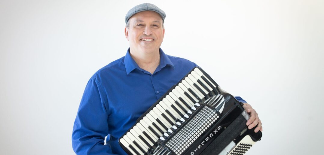 Photo of Steve Normandin sitting and  holding an accordion against a white backdrop.