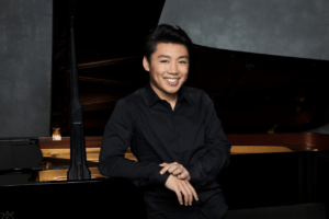 George Li leaning on a grand piano