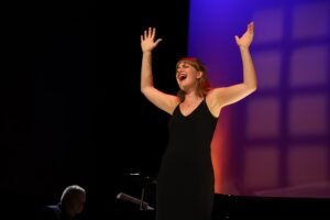Woman singing on stage with her arms in the air