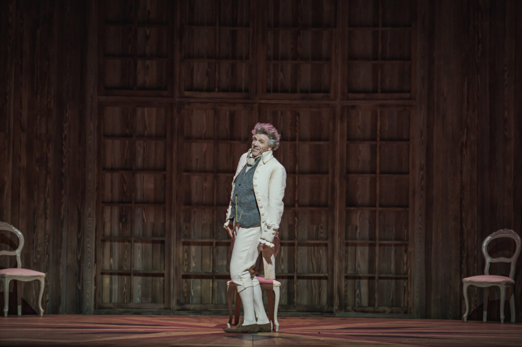 Thomas Hampson in a suit for a costume on stage with three chairs in the background.