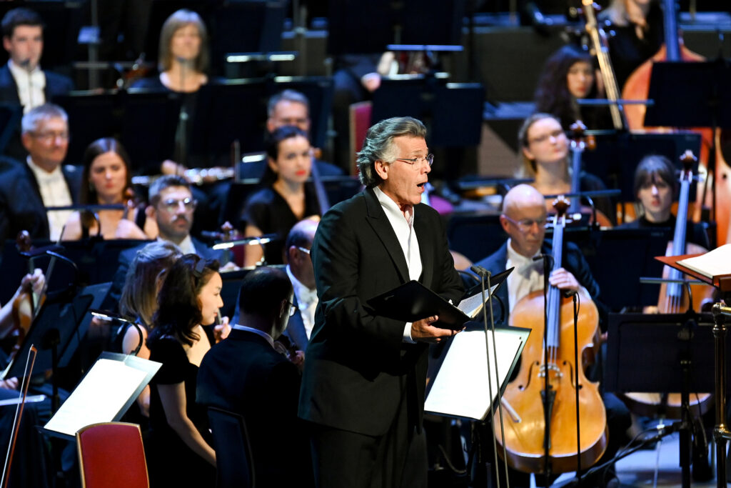 Thomas Hampson singing on stage with a orchestra behind him.