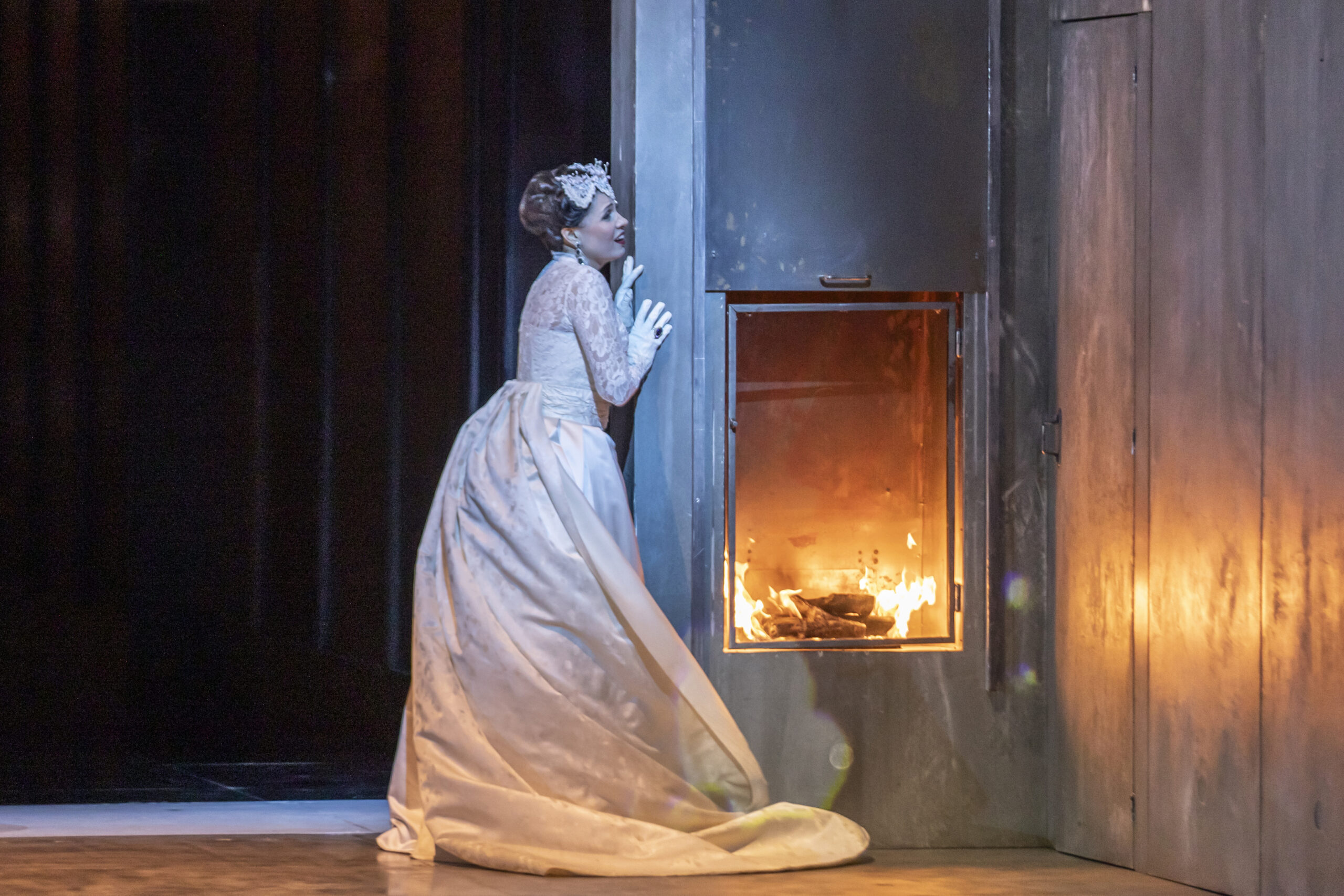 Scene from Opéra national de Paris's 24-25 Don Carlos. A woman stands to the side of a fireplace