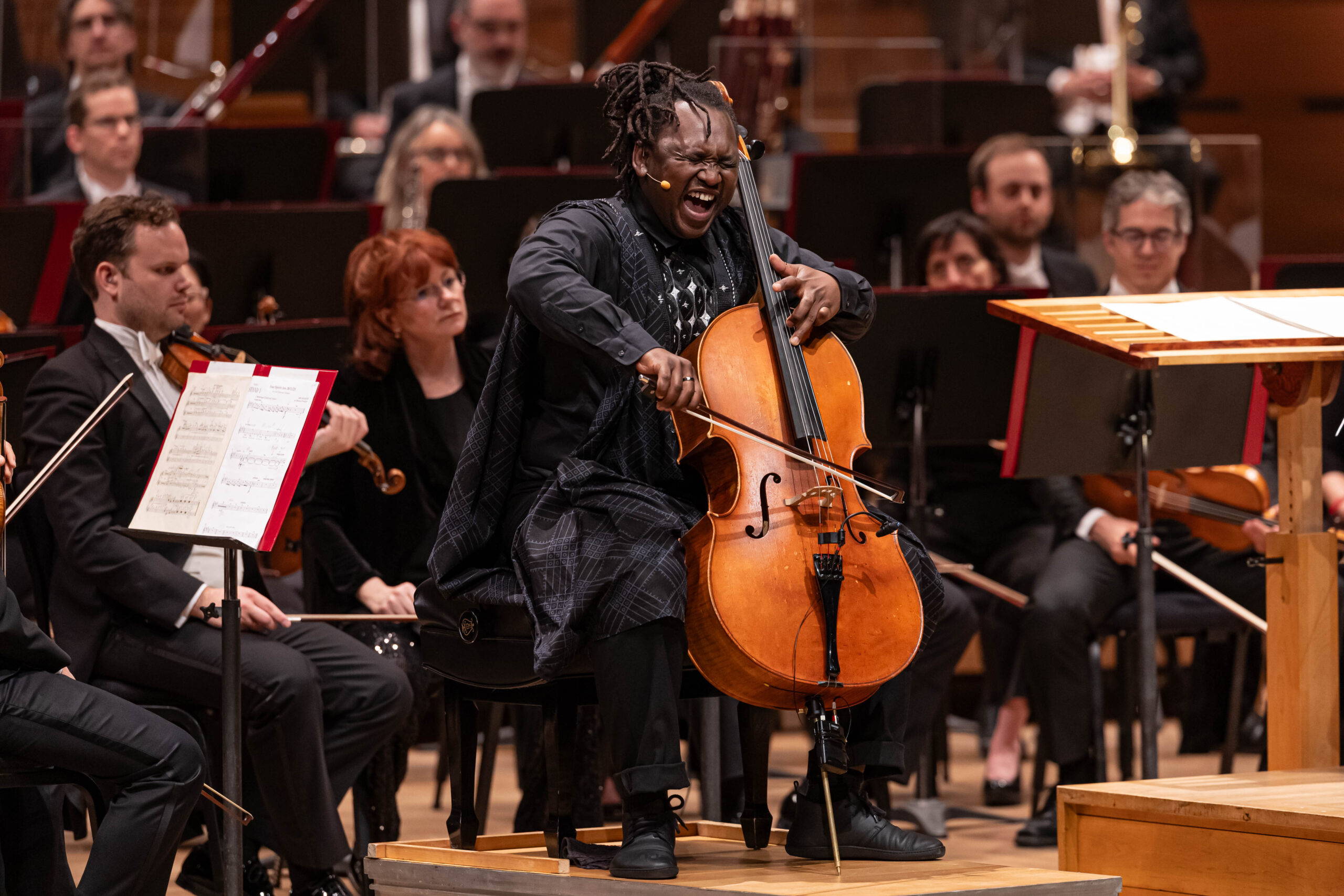 Abel Selaocoe playing the cello with OSM behind him performing Four Spirits