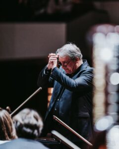 John Storgårds in front of the NAC Orchestra, hands clasped in thanks